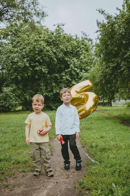 2 boys in the park are photographed in honor of their birthday, against a background of confetti. A boy is photographed with his brother and the number 5 on his birthday.