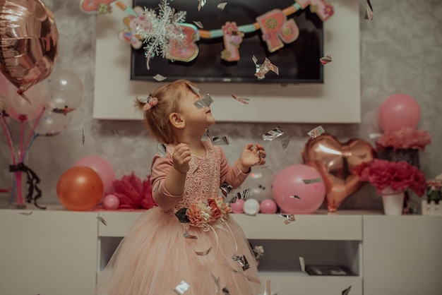 2 year baby girl in pink dress with her first birthday cake, happy birthday card,a cute little girl celebrates her first birthday surrounded by gifts