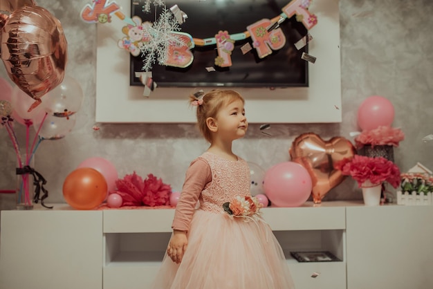 2 year baby girl in pink dress with her first birthday cake happy birthday carda cute little girl celebrates her first birthday surrounded by gifts