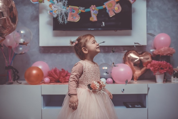 2 year baby girl in pink dress with her first birthday cake happy birthday carda cute little girl celebrates her first birthday surrounded by gifts