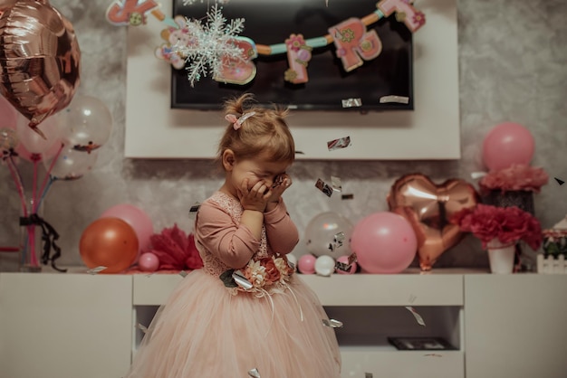 2 year baby girl in pink dress with her first birthday cake happy birthday carda cute little girl celebrates her first birthday surrounded by gifts