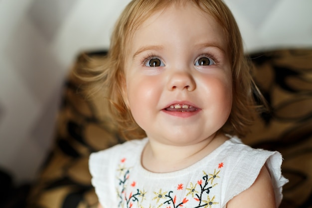 A 2 years old girl is sitting on the bed and smiling. The child rejoices and turns over. Happy child