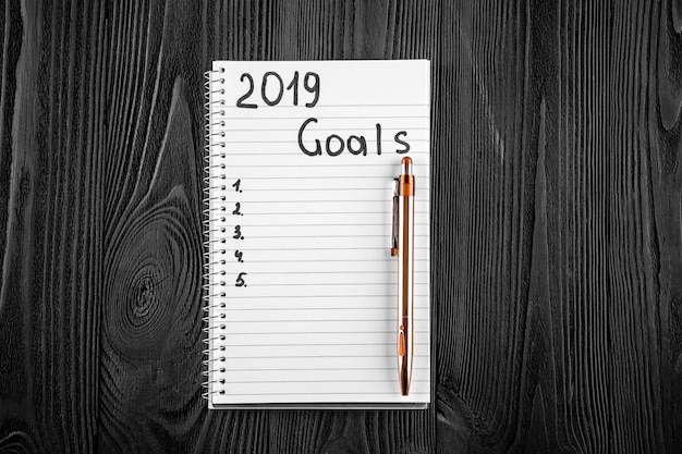 2019 GOALS on his notebook. New year resolutions concept. Top view.