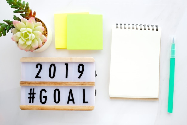 2019 goals on wood box and blank notebook paper on white marble background