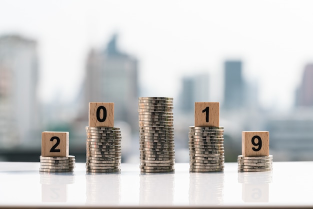 2019 wooden blocks on top of coin stack on city backgrounds.