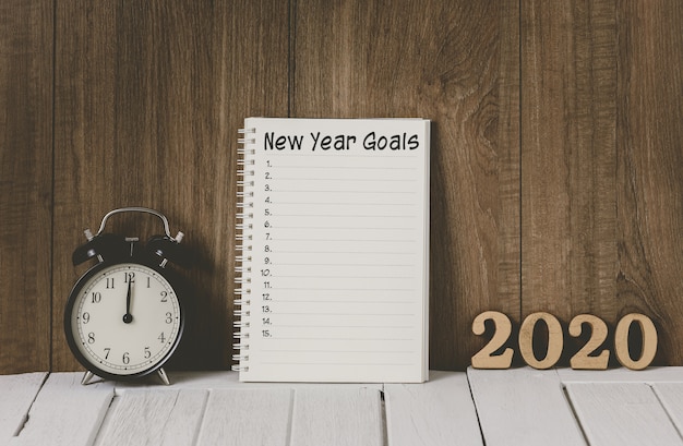 2020 wooden text and New Year's Goals List written on Notebook with Alarm clock