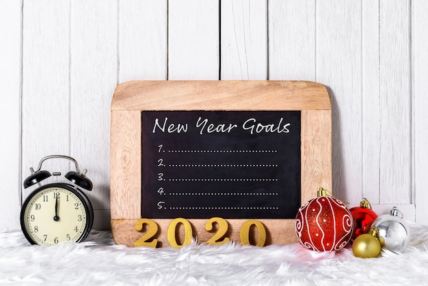 2020 wooden text with Alarm clock with Christmas ornaments and New Year's Goals List written on chalkboard with white fur