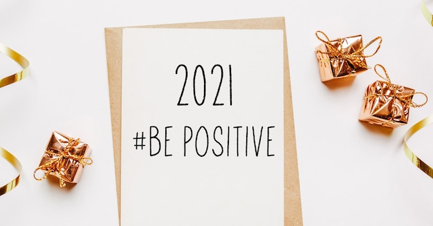 Photo 2021 be positive note with envelope, gifts and gold ribbon on white background. merry christmas and new year concept