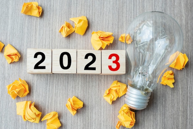 2023 text wood cube blocks and crumbled paper with lightbulb on wooden table background New Year New Ideas Creative Innovation Imagination inspiration Resolution Strategy and goal concept