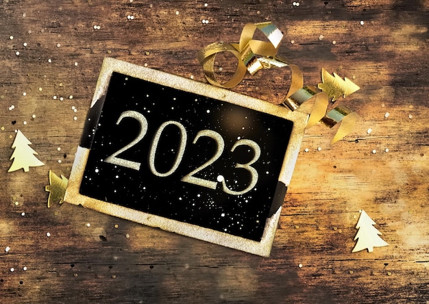 2023 writen on a black little board on illuminated wooden background greetings card for new year