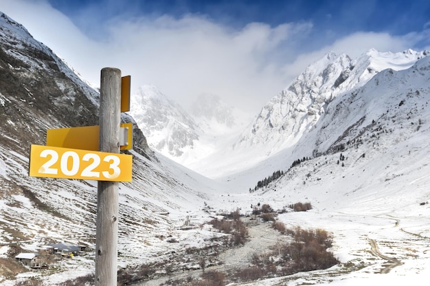 2023 written on yellow postsign on mountain in snow background