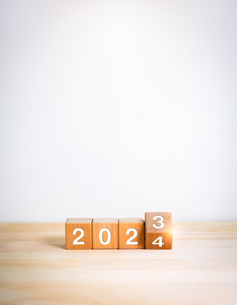 2024 happy new year with change to new era concepts Flipping the 2023 to 2024 year calendar numbers on wooden cube blocks isolated on wood table and white vertical banner background minimal style