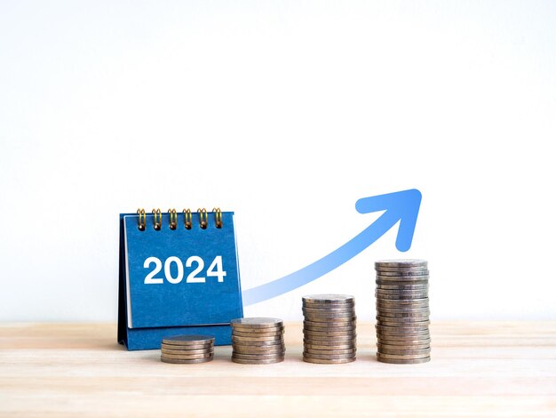 2024 new year goal and success savings business investment and financial concepts Coin stack as a growth graph with big rising arrow near 2024 desk calendar on wooden table and white background