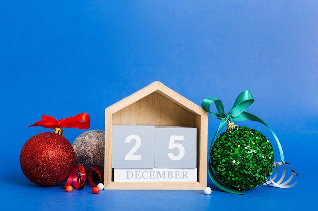 25 december Christmas composition on colored background with a wooden calendar with a gift box toys bauble copy space