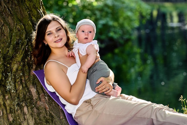 26 years old woman with infant is sitting near tree in park during maternity leave.