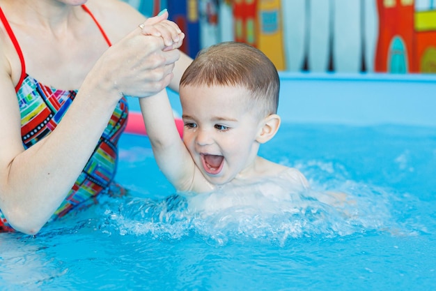 A 2yearold boy learns to swim in a pool with a coach Swimming lessons for children Swimming school for children Educational swimming courses for children