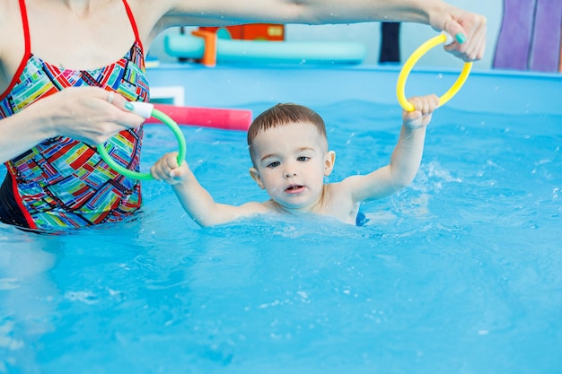 A 2yearold boy learns to swim in a pool with a coach Swimming lessons for children Swimming school for children Educational swimming courses for children