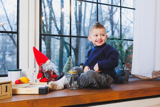 A 2yearold boy sits on the windowsill in the new year New Year's atmosphere at home The child is waiting for the new year