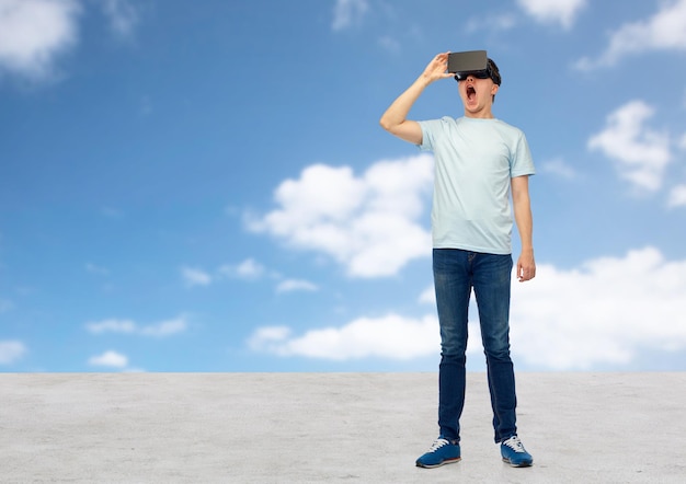 3d technology, virtual reality, entertainment, cyberspace and people concept - amazed young man with virtual reality headset or 3d glasses looking at something over blue sky and clouds background