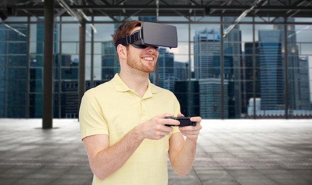 3d technology, virtual reality, entertainment and people concept - happy young man with virtual reality headset or 3d glasses playing with game controller gamepad over empty industrial room