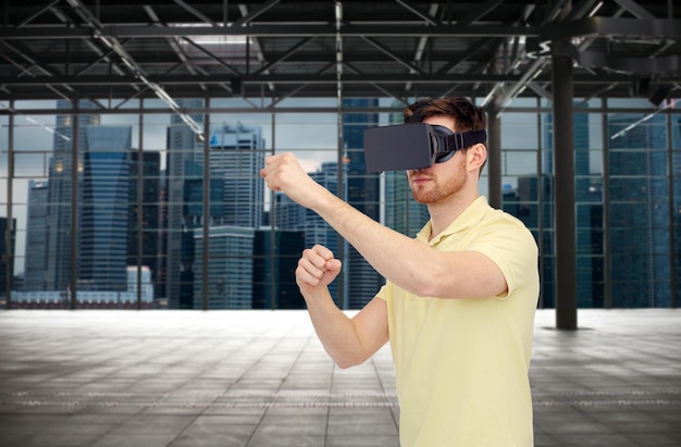 Photo 3d technology, virtual reality, entertainment and people concept - young man with virtual reality headset playing game and fighting over empty industrial room and city panorama background