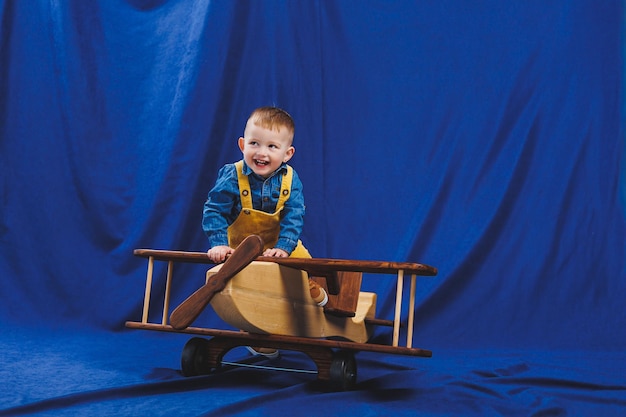 A 3yearold boy in a checkered shirt sits on a large wooden plane Children's environmentally friendly toys from wood