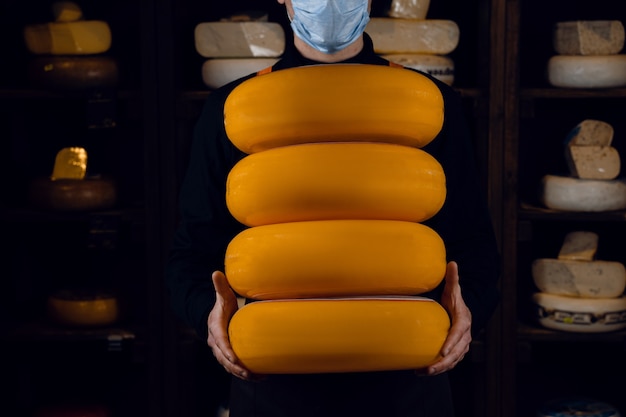 4 Big yellow cheeses wheels in hands. Seller in mask for protection against coronavirus covid-19. holding round cheese.