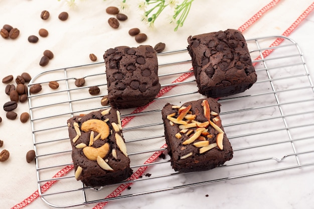 4 square dark brownies with chocolate chips, almonds and nuts on a baking rack, coffee beans placed on a white cloth, top view.