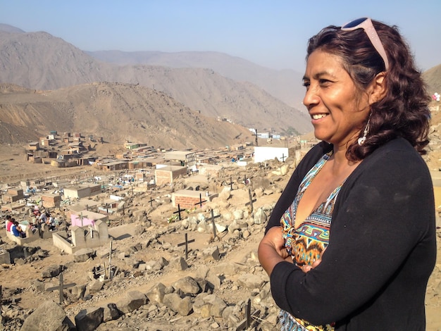 A 40-year-old brunette woman smiling and with her arms crossed from the top of a hill.