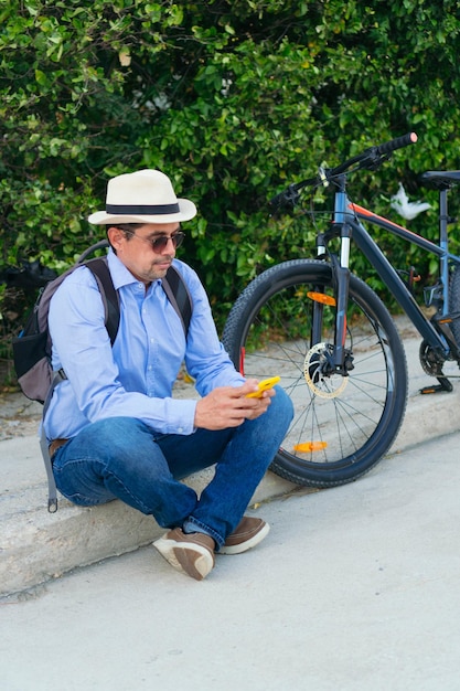 40-year-old man checking his cell phone while sitting on the street with his bicycle