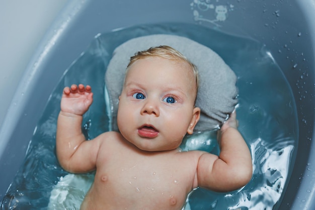 A 4monthold little boy bathes in a bathtub while lying on a stand Caring for a newborn baby bathing the baby