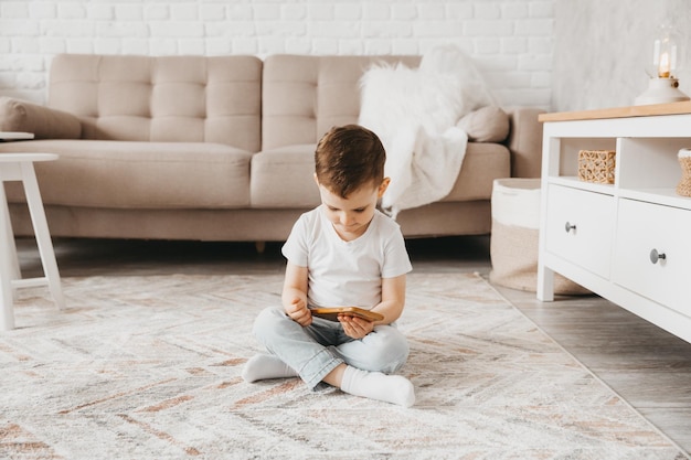 A 5yearold boy looks at a smartphone the child sits on the floor and holds the phone