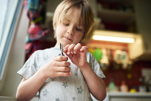 6 year old boy creates crafts at home. He is holding a plier and a wooden stick