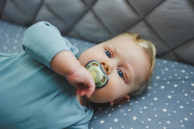 A 6monthold child lies in a crib and looks at the camera Gray bed linen for a baby bed