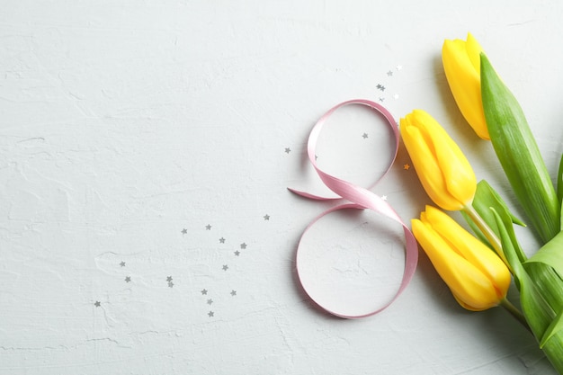 8 March, International Women's Day. Figure eight of pink ribbon with beautiful yellow tulips on gray background. Space for text