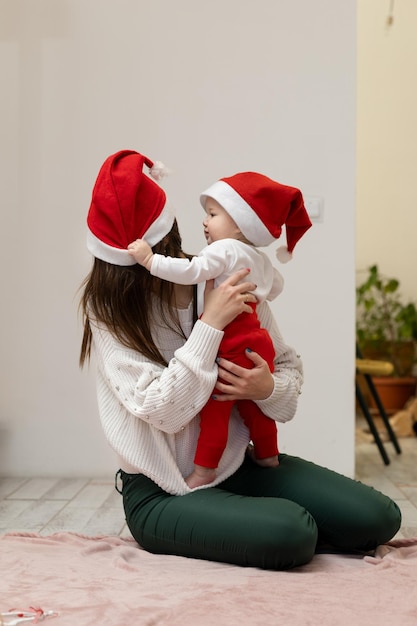 A 9monthold child sitting on his mother's hands pulls off a Christmas hat from his mother's head