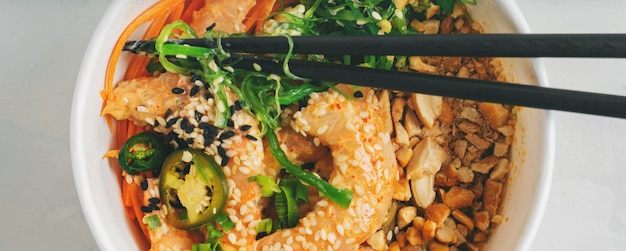 ÃÂ¡lose-up of Spicy Shrimp Poke Bowl with rice, seaweeds and sesame seeds, avocado in a lunch box with chopsticks on white. Healthy seafood lunch. Diet food. Top view with copy space.