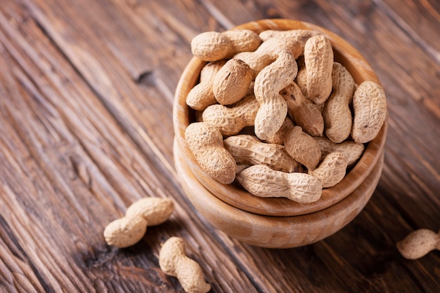 Â Roasted peanuts in wooden bowl on dark, selective focus image