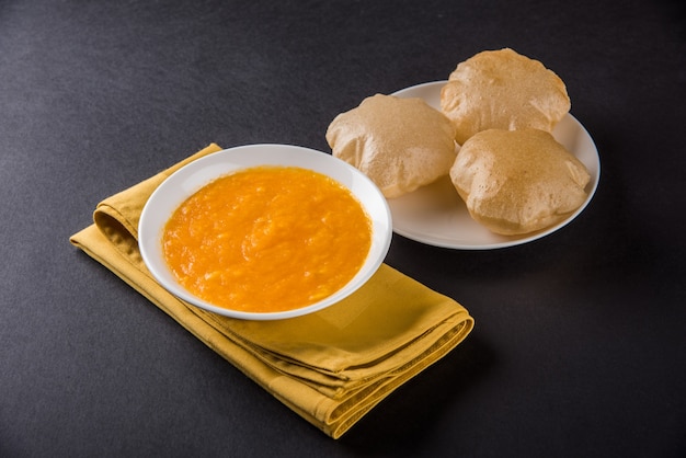 Aam Ras Puri is a delicious Indian recipe served as a seasonal Dessert,  Aamras is plain Mango Puree or Pulp, Served in a ceramic bowl and plate over colourful or wooden background. Selective focus