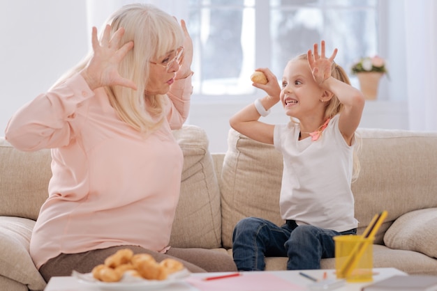 Absolutely funny. Nice pretty joyful girl smiling and looking at her grandmother while playing with her