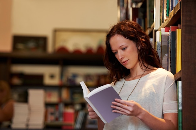 Absorbed in the plot A young woman lost in the pages of a novel against a backdrop of full bookshelves