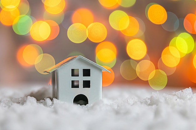 Abstract advent christmas background toy model house on snow with defocused garland lights backgroun