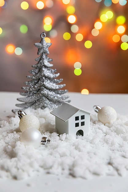 Abstract Advent Christmas Background Toy model house and winter decorations ornaments on background with snow and defocused garland lights Christmas with family at home concept