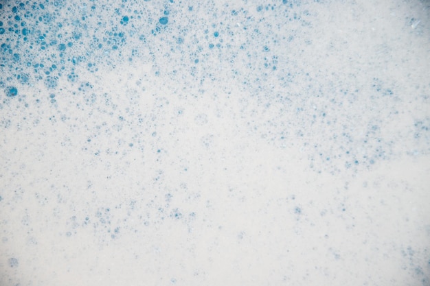 Abstract background texture of white soap foam. Shampoo foam with bubbles on a blue background. Detergents and hygiene.