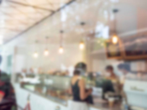 Abstract blurred background inside the coffee shop and the counter bar Blurry bright cafe with people and hanging lamp with bokeh light