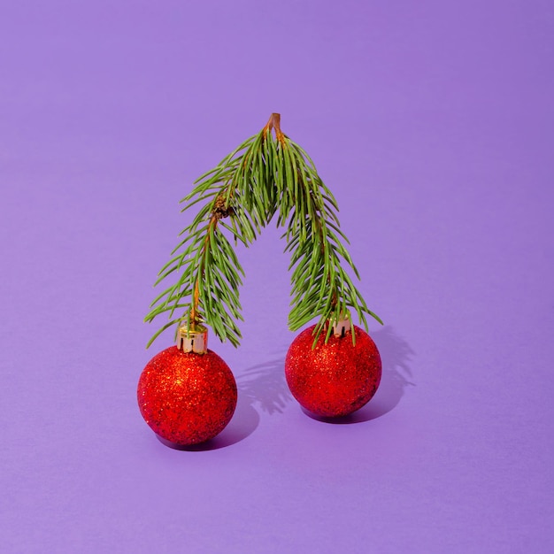 Abstract cherry decoration with green pine branches and red balls placed on a pastel purple background. Shiny cherry glitter as Christmas tree decoration. Sweet fruit shiny balls with shadows.