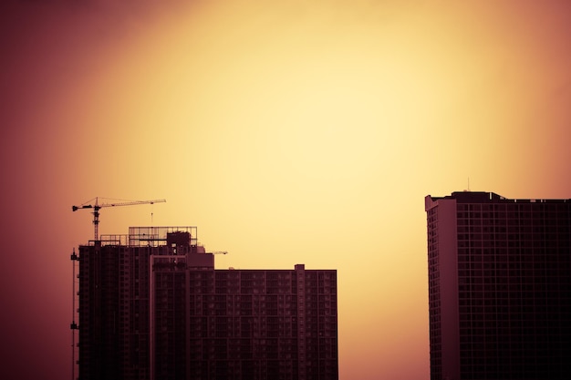 Abstract construction cranes and building silhouettes over sun at sunrise vintage picture tone