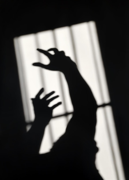 Abstract dark shadow on wall concept hands behind prison fence seek to freedom