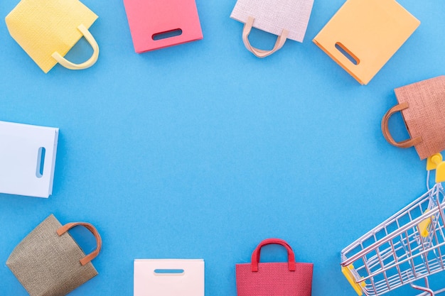 Photo abstract design element, annual sale, shopping season concept, mini yellow cart with colorful paper bag on pastel blue background, top view, flat lay