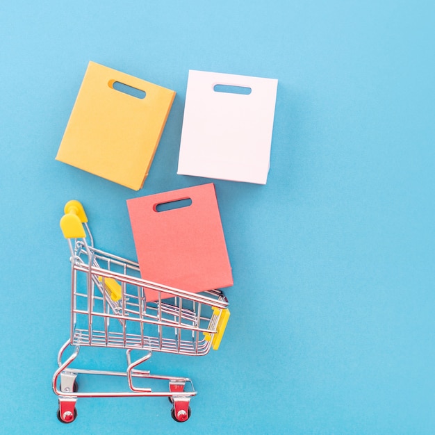 Photo abstract design element, annual sale, shopping season concept, mini yellow cart with colorful paper bag on pastel blue background, top view, flat lay